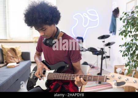 Young serious man with headphones around his neck playing electric guitar while sitting in home environment Stock Photo