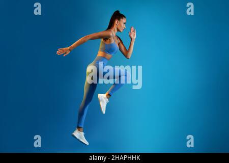 Sporty Woman Exercising Doing Elbow-To-Knee Crunch Standing On Blue Background Stock Photo