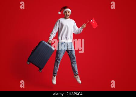 Turkey Tours. Man In Santa Hat Jumping With Turkish Flag And Suitcase Stock Photo