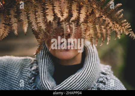 Concept of nature and environment save the world. Close up portrait of woman hidden his face with dry autumn leaf in front of her face. Park and green Stock Photo