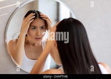 Worried long-haired chinese woman checking her hair Stock Photo