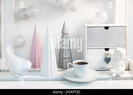 Ceramic figurines of pastel-colored Christmas trees, a white faience angel, a garland of balls made of threads decorate the room before Christmas Stock Photo