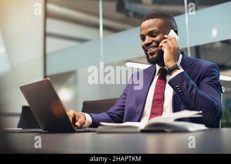 Successful black businessman working on laptop, having phone conversation Stock Photo