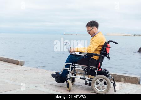 a man with disabilities in a wheelchair works on a computer on the Internet Stock Photo