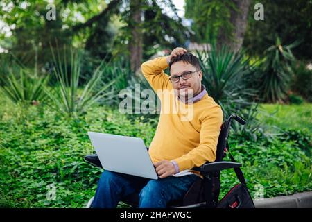 a man with disabilities in a wheelchair works at a computer on the Internet Stock Photo
