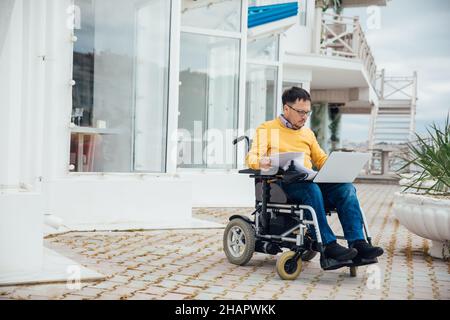 a man with disabilities in a wheelchair works at a computer on the Internet Stock Photo