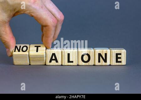 You are not alone symbol. Businessman turns wooden cubes and changes words alone to not alone. Beautiful grey table grey background, copy space. Busin Stock Photo