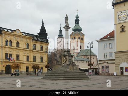 Plague Column in the SNP Square in Banská Bystrica, Slovakia. The medieval barbican with the clock tower is seen in the background at the right while the Church of the Assumption (Kostol Nanebovzatia Panny Márie) is seen at the left. Stock Photo