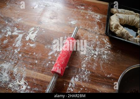 Vegan apple strudel in a baking tray on a table dusted with flour and red rolling pin on its work surface. Stock Photo