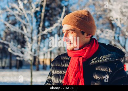 Portrait of young man in snowy winter park wearing warm clothes feeling cold walking outdoors. Seasonal activities Stock Photo