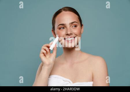 Ginger woman wearing towel smiling and showing lipbalm isolated over blue background Stock Photo