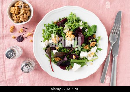 Healthy salad with beets, walnuts, arugula and feta cheese on white plate, pink textile background, top view Stock Photo