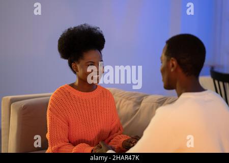 Young african couple sitting on sofa and holding hands, black man and woman expressing love, empathy Stock Photo