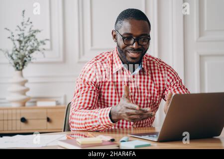 Positive african man online teacher tutor looking at laptop screen and talking with students Stock Photo