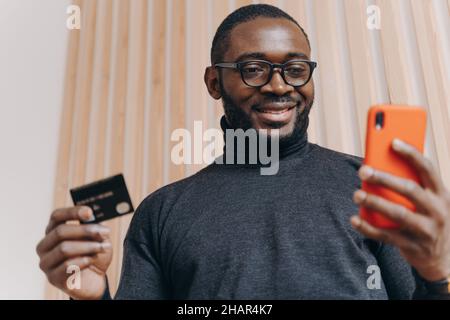 Cheerful African american businessman holding credit card and smartphone for shopping in internet Stock Photo