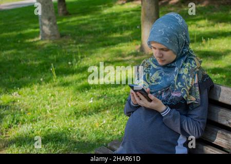 Muslim pregnant woman using smartphone in the park Stock Photo