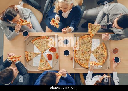 Top view of business people in formal wear sitting at table and having pizza for lunch. Stock Photo