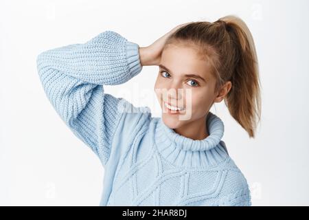 Close up portrait of beautifu teen girl, child posing in ponytail, wearing winter sweater and smiling, standing against white background Stock Photo