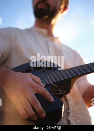 upward focus on a man holding a guitar and covering the sun Stock Photo