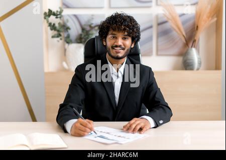 Headshot successful positive Indian business man, financial consultant, talking with colleague or client via video link, conducting virtual interview, looking at camera, taking notes, smiling Stock Photo