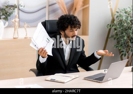 Emotional, angry annoyed Indian ceo, business leader or manager, with a beard, have bad conversation with an online communication colleague, displeased facial expression, hand gestures Stock Photo