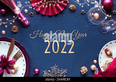 Happy New Year 2021 gilded text in frame with New Year party table setup. Golden, pink and red decor on linen textile. Stock Photo