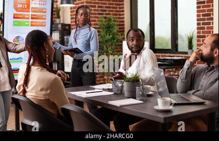 Businesswoman explaining management strategy showing company graph on monitor discussing business collaboration with businessteam. Diverse entrepreneurs working at project in startup office Stock Photo