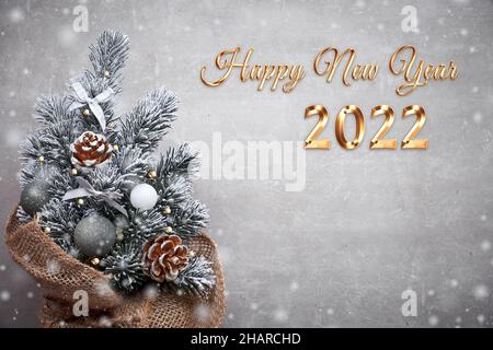 2022 Happy New Year text. Small Christmas tree in sackcloth decorated with red baubles and berries on light stone with copy-space Stock Photo