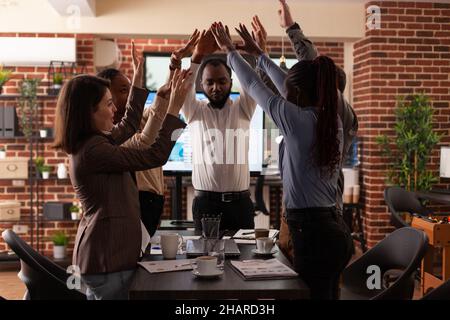 Successful excited diverse businesspeople celebrating winning business partnership rising hands while working in startup company office. Happy businessteam enjoying triumph at workplace Stock Photo