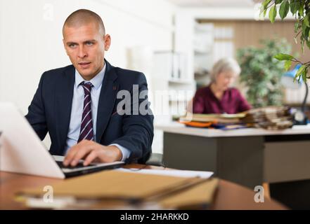 Focused businessman working with laptop at table in office Stock Photo