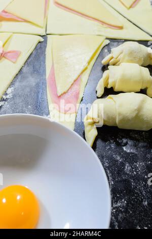 Vertical shot of preparations of croissants, stuffed with ham and cheese and painted with egg yolk Stock Photo