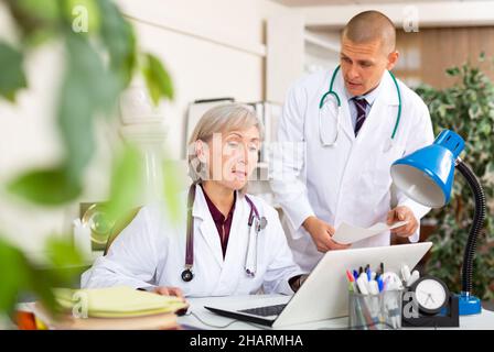 Two physicians working with case histories on laptop in office Stock Photo