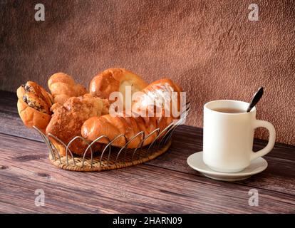 An assortment of homemade cakes on a decorative tray and a cup of hot black tea on a wooden table. Close-up.