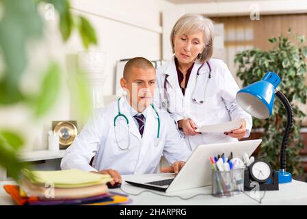 Two physicians working with case histories on laptop in office Stock Photo