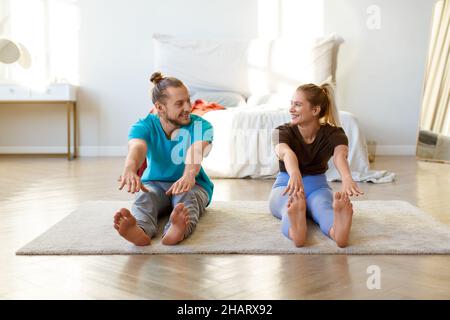 A young couple is doing stretching together at home. She look at each other and smile. Stock Photo