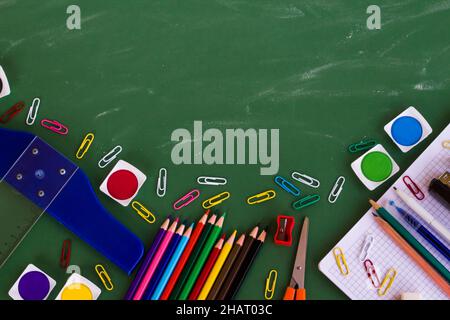 Colorful school supplies on greenboard with chalk dust trail and copy space. Stock Photo
