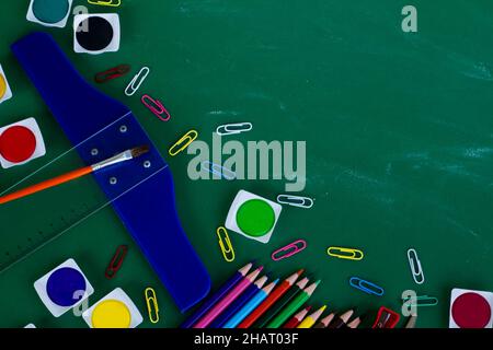 Colorful school supplies on greenboard with chalk dust trail and copy space. Stock Photo