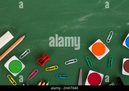 Colorful school supplies on greenboard with chalk dust trail and copy space. Stock Photo