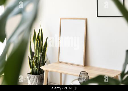 Blank frame on wooden table and houseplant near light wall Stock Photo