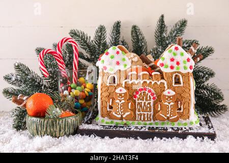 Board with beautiful gingerbread house, tangerines, snow and treats on white wooden background Stock Photo