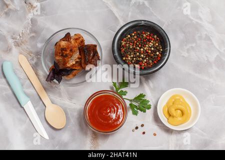 Grilled pork in a glass bowl with fresh basil. Bowls with ketchup and mustard, a stone bowl with spices. Top view. Stock Photo