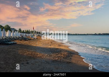 Beach views, Sun loungers, umbrellas, flags and small wavy coastline in Antalya Side. Selective Focus. Stock Photo