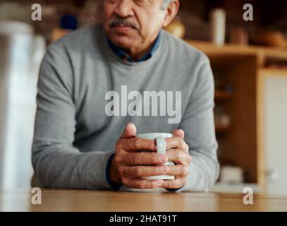 Close up of hands of pensive retired biracial elderly male leaning on modern kitchen counter, holding morning coffee in his hands. Stock Photo