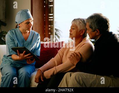 Medical professional explaining diagnosis to elderly multi-ethnic couple in at-home consultation Stock Photo