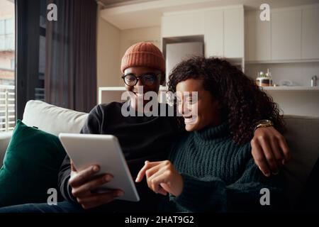 Adult couple, multi-ethnic, smiling while using tabe on sofa in modern apartment Stock Photo