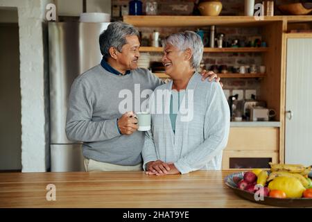 Loving retired elderly biracial couple laughing at each other while standing in modern kitchen. Stock Photo