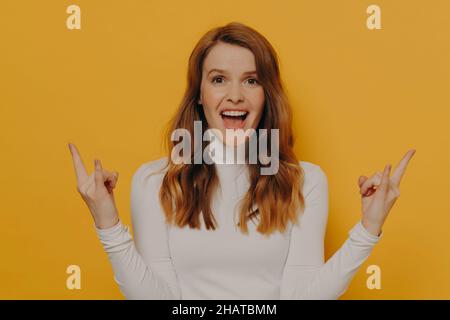 Carefree teen girl with brown wavy hair and pierced tongue showing rock and roll gesture or sign of horns Stock Photo