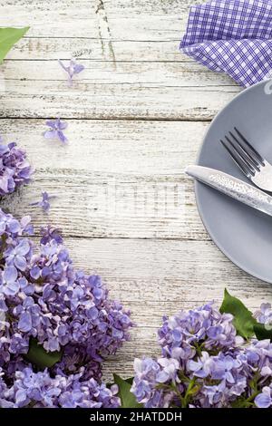 spring table setting with plate fork and knife decorated with lilac flowers on white wooden background. Top view with copy space in very peri trendy c Stock Photo