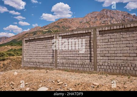 An unfinished, rough concrete block wall being constructed around a house up in the mountains. In the Lake Charvak resevoir area near Tashkent, Uzbeki Stock Photo