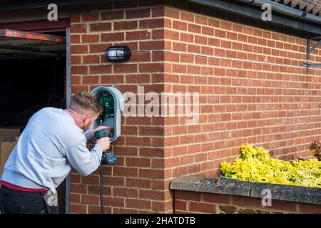 Electrician fitting a Zappi electric car charger to the outside wall of a private garage. NB:  The premises in the photograph are Property Released. Stock Photo